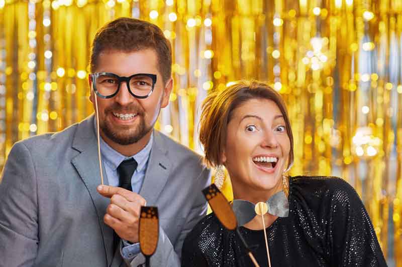 Couple posing with gold tinsel backdrop and photo booth props